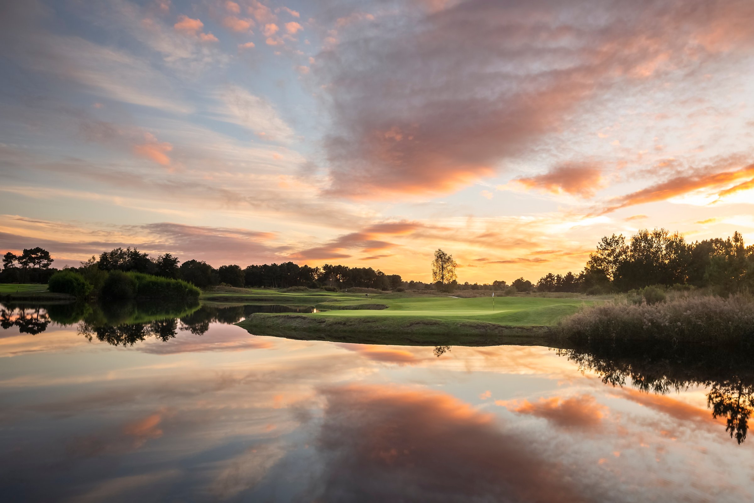 Parcours de golf de Cabot Bordeaux au coucher du soleil, ciel rose et orangé reflété dans un étang