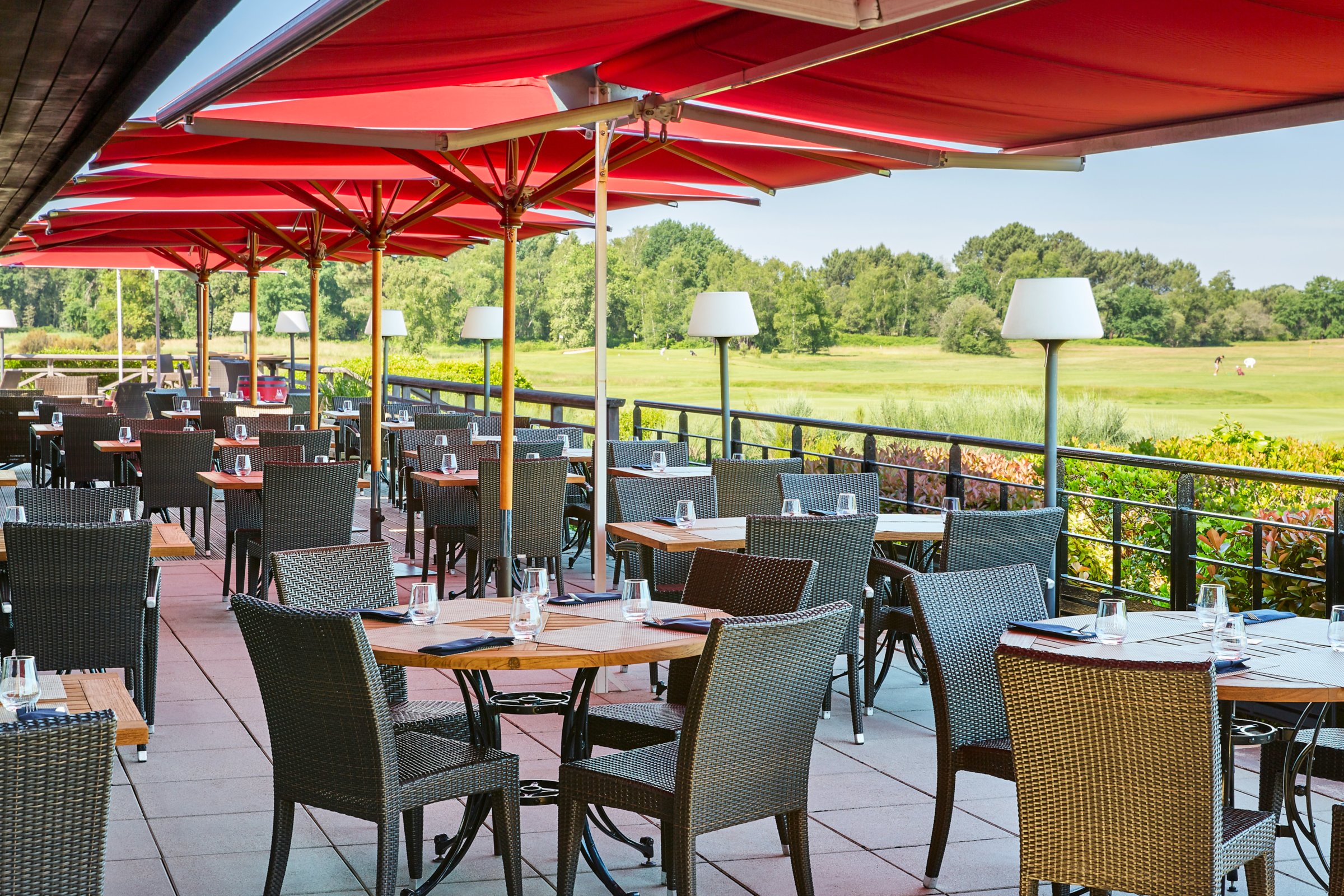 Terrasse du restaurant de Cabot Bordeaux, parasols rouges et tables dressées face au parcours de golf