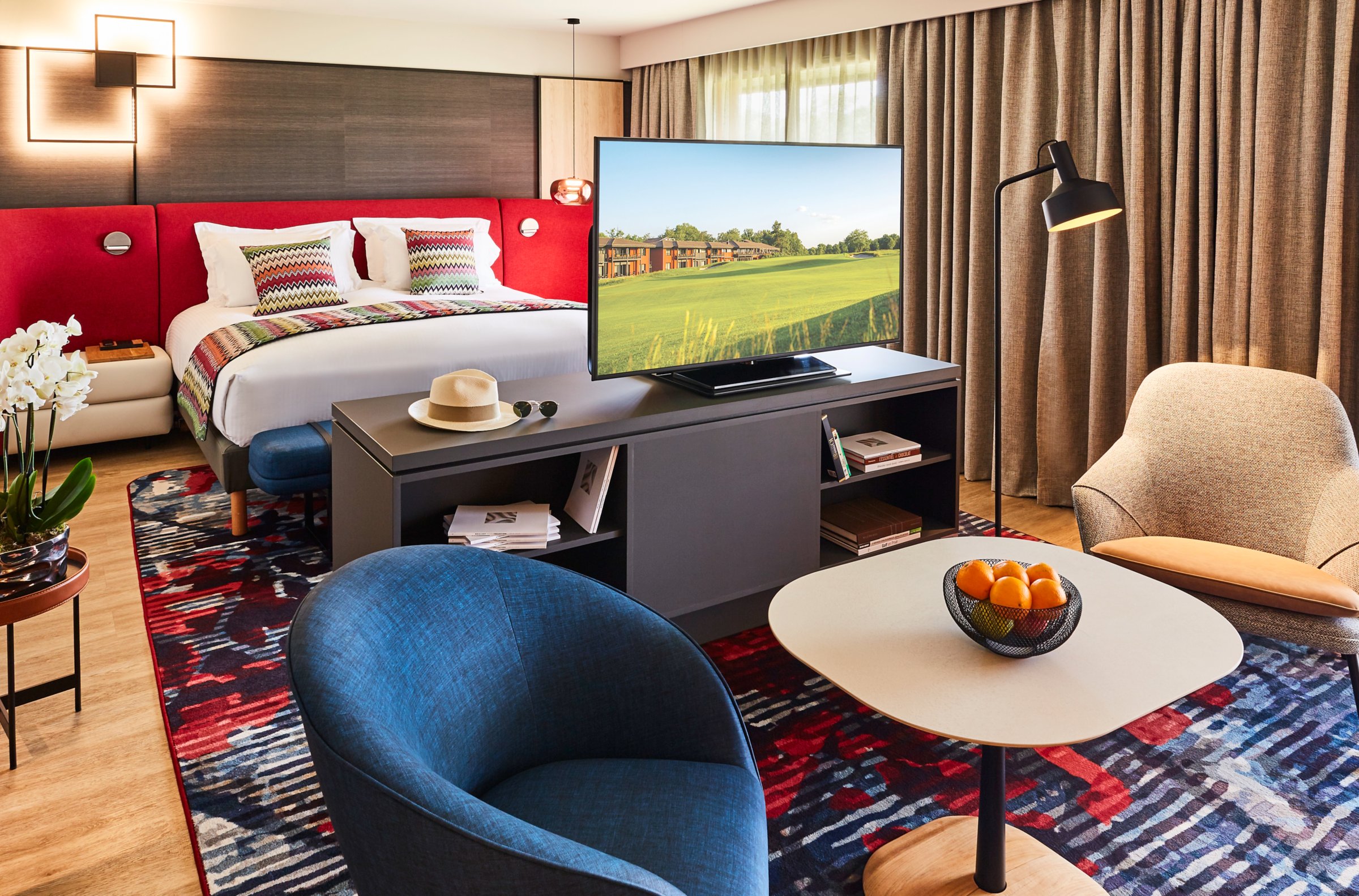Suite de Cabot Bordeaux avec lit king size, tête de lit rouge, coin salon et vue sur le golf