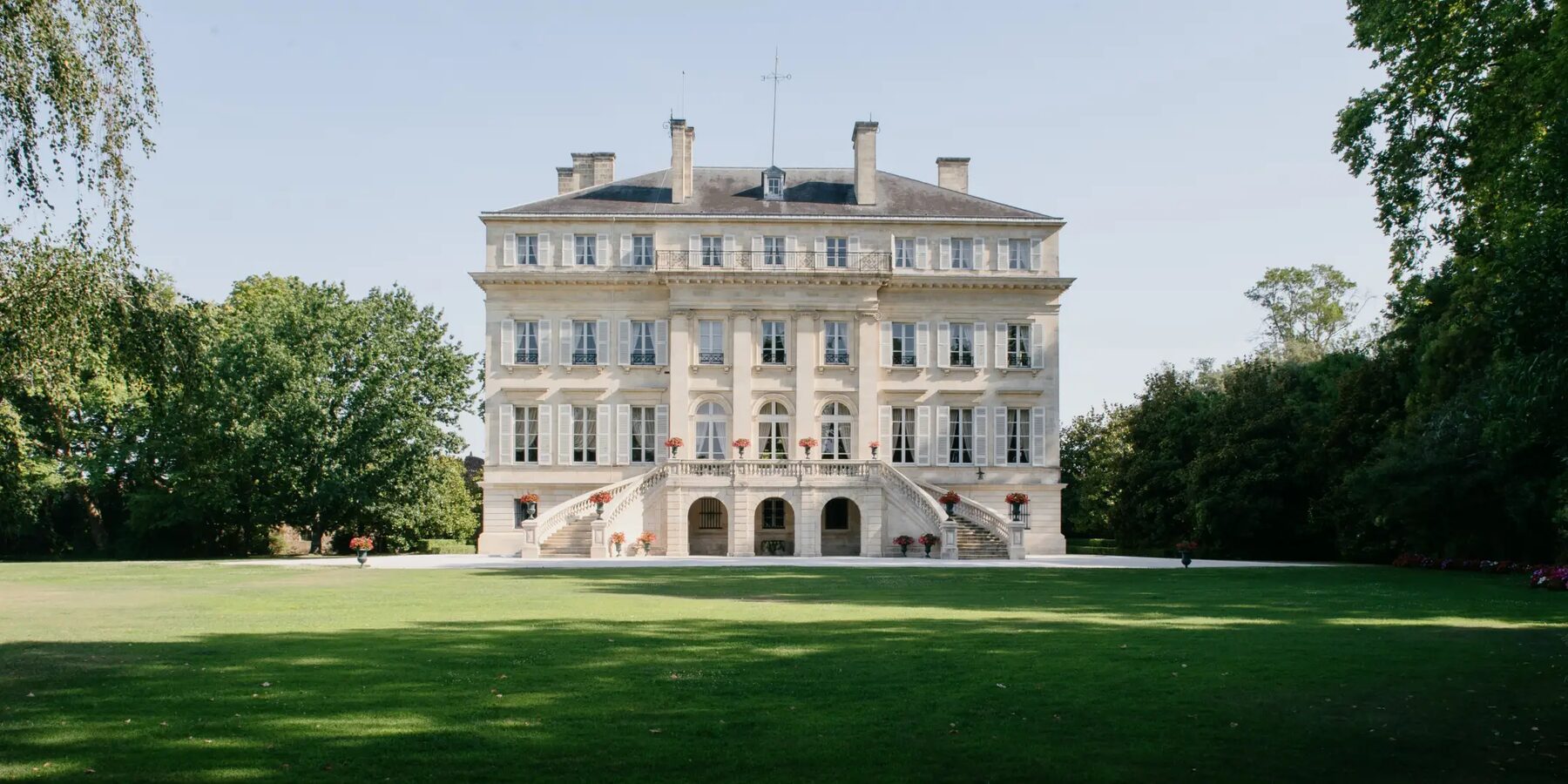 La façade néoclassique de Château Margaux, son double escalier et sa pelouse, entre les arbres du parc