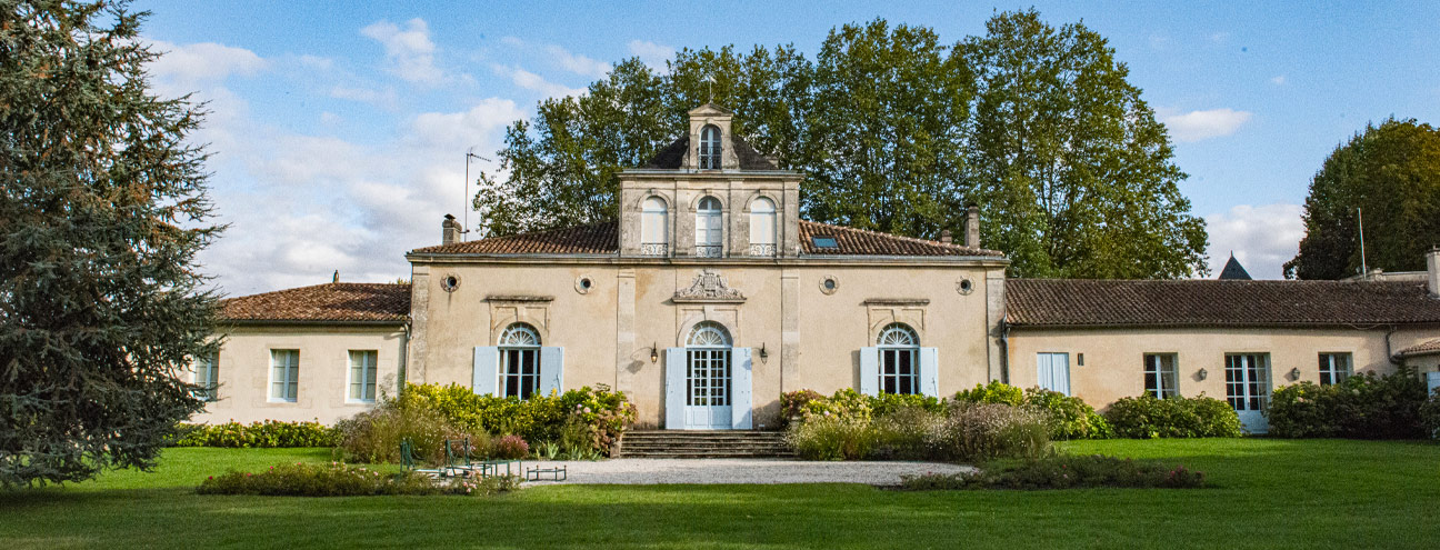 La façade du Château Siran, ses volets bleus et sa pelouse sous un ciel bleu, à Labarde dans l'appellation Margaux